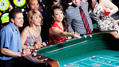 Woman throwing dice at craps table with a crowd around her.